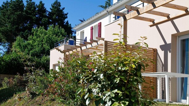 A residential building with a wooden pergola, a balcony, and a garden with various plants. - Apartment in Bretagne near Morbihan Coast (BADEN)