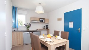 A compact kitchen with modern appliances, a dining table set for two with a fruit bowl, and a blue door. - Apartment in Bretagne near Morbihan Coast (BADEN)