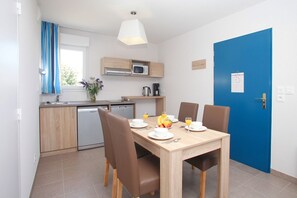 A compact kitchen with modern appliances, a dining table set for two with a fruit bowl, and a blue door. - Apartment in Bretagne near Morbihan Coast (BADEN)