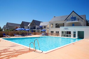 A swimming pool with sun loungers and umbrellas, surrounded by buildings with balconies.