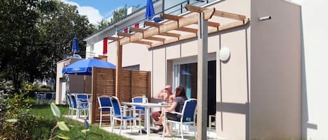 An outdoor seating area with tables and chairs, a wooden pergola, and umbrellas.