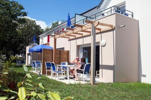 An outdoor seating area with tables and chairs, a wooden pergola, and umbrellas.