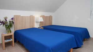 A hotel room with two beds, a nightstand with a lamp, and a small table with a vase of flowers. - Apartment in Bretagne near Morbihan Coast (BADEN)