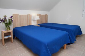 A hotel room with two beds, a nightstand with a lamp, and a small table with a vase of flowers. - Apartment in Bretagne near Morbihan Coast (BADEN)