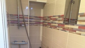 Una ducha a ras de suelo con mampara de vidrio, paredes alicatadas y cabezal de ducha.