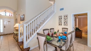 A dining area with a glass table and chairs, a staircase, and wall decor. - Spacious Villa In Emerald Island Resort, Kissimmee / Orlando, Florida, USA (Kissimmee)