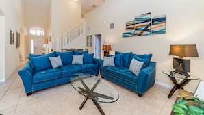 A spacious living room with two blue sofas, a glass coffee table, and a staircase leading to another level. - Spacious Villa In Emerald Island Resort, Kissimmee / Orlando, Florida, USA (Kissimmee)