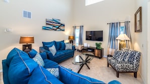 A living room with a blue sofa, a patterned armchair, a glass coffee table, and a flat-screen TV mounted on the wall. - Spacious Villa In Emerald Island Resort, Kissimmee / Orlando, Florida, USA (Kissimmee)