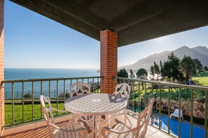 A balcony with a table and chairs, overlooking a pool and a mountainous landscape.