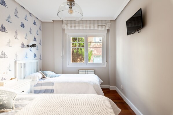 A bedroom with two beds, a window with a view, a radiator, and a TV mounted on the wall.
