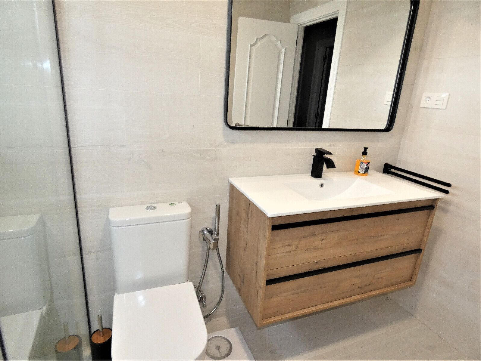 Un baño moderno con un inodoro blanco, un tocador de madera con un lavamanos y un espejo sobre el tocador.