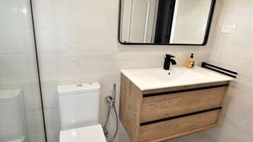 Un baño moderno con un inodoro blanco, un tocador de madera con un lavamanos y un espejo sobre el tocador.