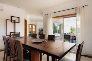A dining area with a wooden table, chairs, and a decorative plate. There is a door leading to a balcony with outdoor seating. - Villa Marazul Quinta Amizade with ocean views, game room, and saltwater pool (Guia)