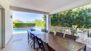 A covered outdoor dining area with a pool view, a wooden table, and chairs. - Villa Marazul Quinta Amizade w/ Sea View, Games room, Salt pool (Guia)