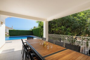 Una mesa de madera con sillas, una piscina y vista al mar.