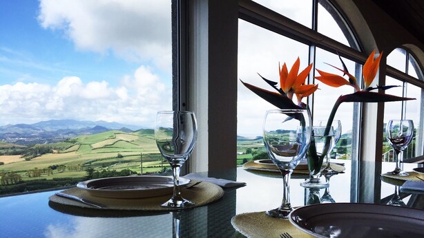 Une table dressée pour le dîner, avec une vue sur des collines verdoyantes et un ciel dégagé.