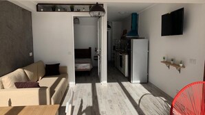 A modern living space with a sofa, a dining table, a red chair, a kitchen area, and a TV mounted on the wall. - Residence Playa Roca Costa Teguise "LANZAROTE" (Costa Teguise)