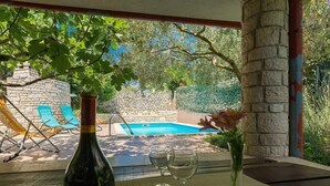 A bottle of wine, two glasses, and a vase with flowers on a table with a view of a swimming pool and lounge chairs. - Stunning  villa for 6 guests with pool, A/C, WIFI, TV, terrace and pets allowed (Krnica)