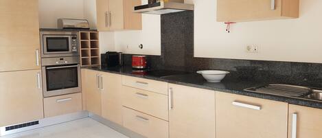 A modern kitchen with wooden cabinets, a built-in oven, a microwave, a coffee machine, and a bowl on the countertop.
