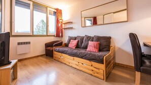 Una habitación acogedora con un sofá de madera, un escritorio pequeño, una silla y un ventanal con cortinas.