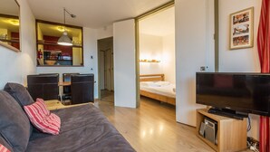 Un espacio habitable pequeño con sofá, cama, televisor y kitchenette.