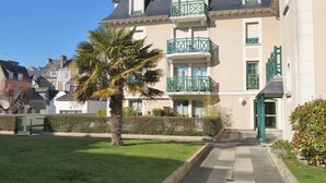 Un edificio a più piani con un balcone, una palma e un vialetto che conduce all'ingresso.