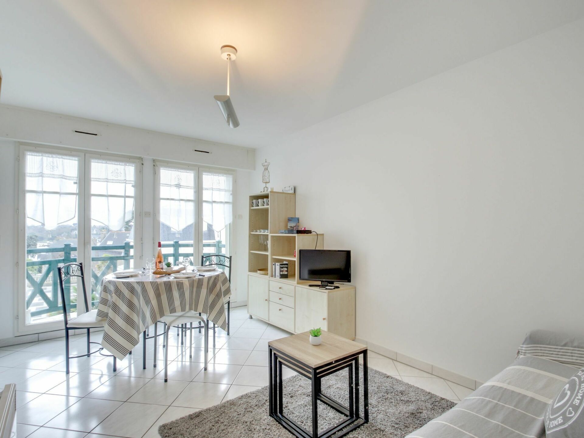 A modern living room with a dining area, a TV on a wooden cabinet, and a balcony with a view.