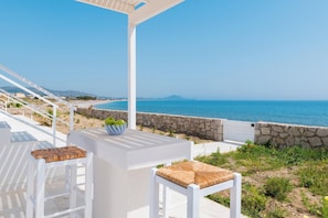 Une terrasse avec des meubles blancs, un mur en pierre et une vue sur la mer.
