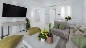 En moderne stue med et fladskærms-tv, en sofa, et sofabord med planter og et spiseområde i baggrunden.