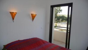 A bedroom with a bed, two wall-mounted lights, and a sliding glass door leading to an outdoor area.