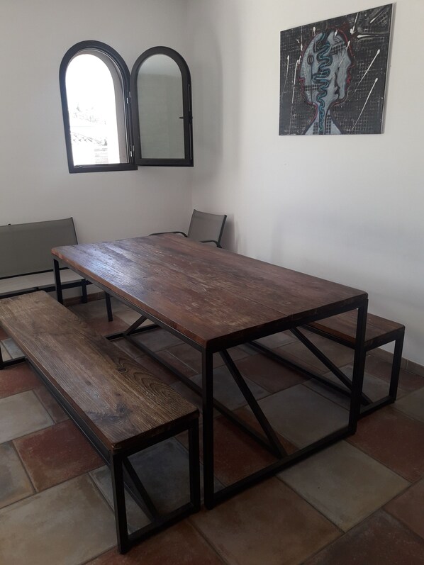 Uma sala de conferência com uma longa mesa de madeira e bancos, duas janelas em arco e uma obra de arte abstrata na parede.