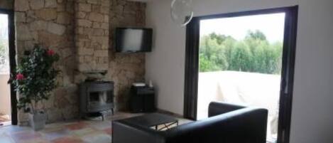 A living room with a stone wall, a fireplace, a flat-screen TV, and a large sliding glass door leading to a balcony.