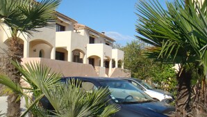 A building with multiple balconies and arched windows, surrounded by palm trees.