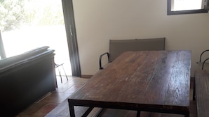A dining table with a bench, a window with a view, and a tiled floor.
