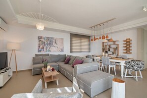 Una sala de estar moderna con un sofá gris, una mesa de centro, un televisor y un comedor con una mesa y sillas de madera.