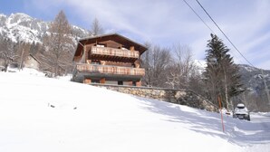 Eine Holzhütte mit Steinfundament, mehreren Balkonen und einer Skipiste im Hintergrund.