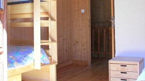 Ein Zimmer mit einem Holzbett mit Etagen, einem kleinen Schreibtisch und Schubladen, einer Tür zu einem anderen Raum und einer Deckenleuchte.
