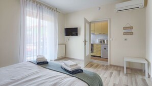 Un dormitorio con una cama, un televisor montado en la pared y una kitchenette en la habitación contigua.