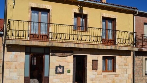 A two-story building with a yellow facade, stone base, and a balcony with metal railings. - Bocanegra Rural Cottage for 10 people (Canicosa de la Sierra)