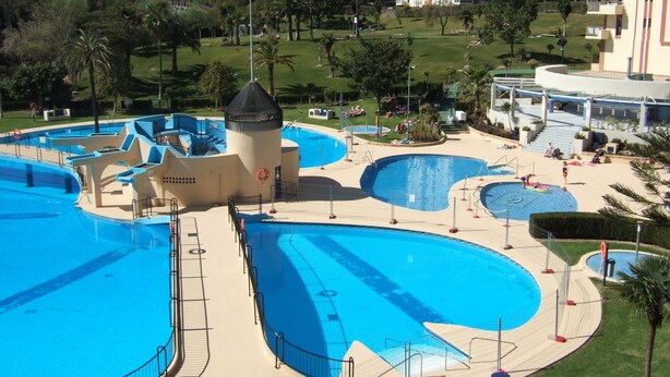 A large outdoor swimming pool complex with multiple pools and a central tower structure. - A beautiful studio apt overlooking pools ' Minerva.Jupiter @ Bonanza Square ' (Benalmadena)