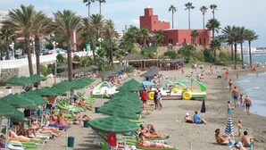 A beach with rows of sun loungers and umbrellas, a water slide, and a red building in the background. - A beautiful studio apt overlooking pools ' Minerva.Jupiter @ Bonanza Square ' (Benalmadena)