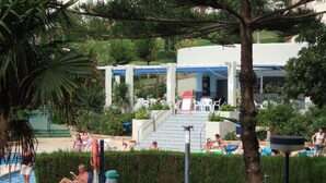 A pool area with lounge chairs, a small pool, and a building with a blue roof in the background. - A beautiful studio apt overlooking pools ' Minerva.Jupiter @ Bonanza Square ' (Benalmadena)