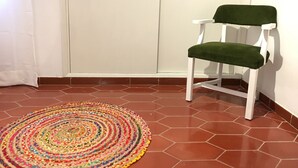 Ein Zimmer mit einer weißen Tür, einem grün gepolsterten Stuhl und einem farbenfrohen Teppich auf einem sechseckigen Fliesenboden.