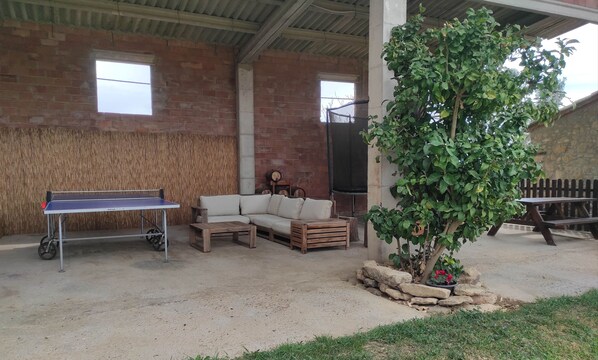 A covered outdoor area with a ping pong table, a sofa, and a small tree.