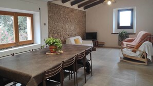 Un espace repas comprenant une grande table, des chaises, un téléviseur et un coin salon confortable avec un fauteuil et une couverture.