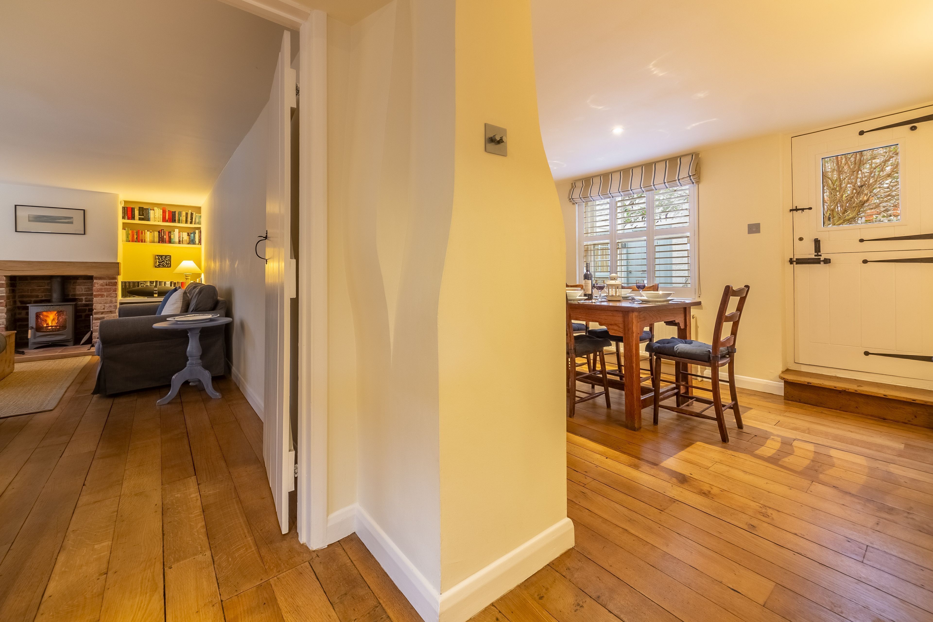 A cozy living room with a fireplace, a bookshelf, and a dining area with wooden flooring and chairs.