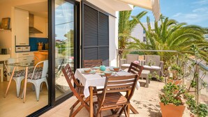 Un área de comedor al aire libre con una mesa preparada para cuatro personas, rodeada de sillas de mimbre y una mesa de vidrio.