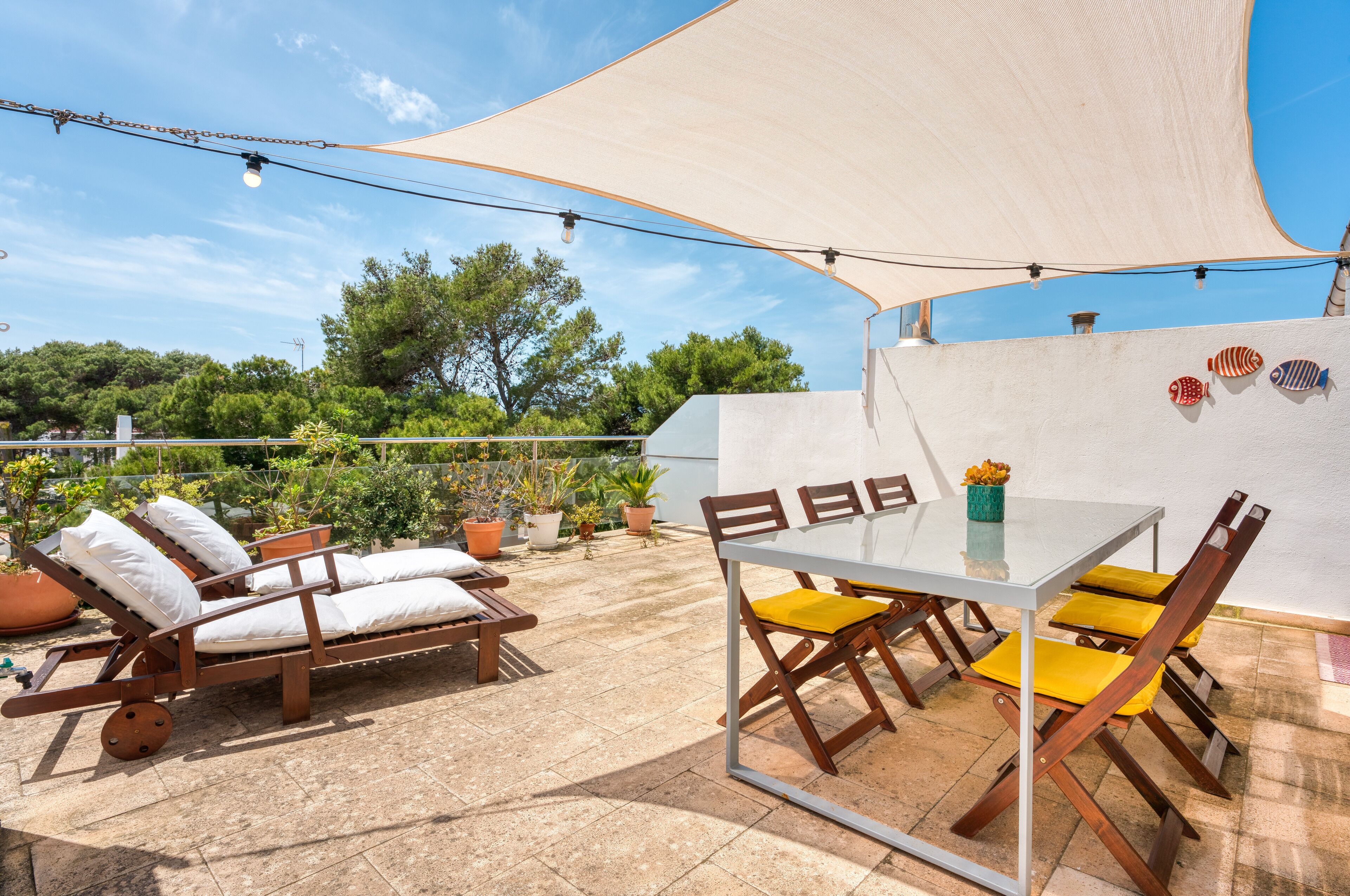 An outdoor patio with a table and chairs, a sun lounger, and a large canopy.