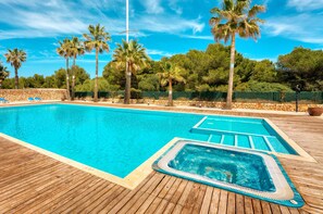 A swimming pool with a wooden deck, surrounded by palm trees and a stone wall. - SPECTACULAR PENTHOUSE-DUPLEX WITH LARGE TERRACE, SWIMMING POOL AND NEXT TO THE SEA (Son Carrió)