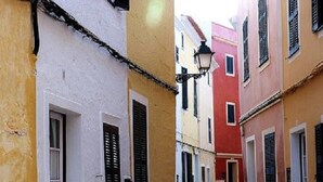 Una estrecha calle adoquinada flanqueada por edificios coloridos, cada uno con contraventanas y un estilo arquitectónico europeo tradicional.
